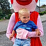 child, boy, mascot, pink_pig, costume, outdoor, blue_sky, grass, trees, casual_clothing, jeans, sneakers, smile, holding, person, fun, playful, daytime, portrait, character
