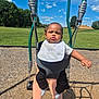 baby, child, swing, playground, outdoor, grass, sky, clouds, bib, socks, person, seat, play, park, fun, daytime, trees, expression, legs, sunny