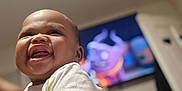 Ja'Leir joined the competition — help win amazing prizes! baby, child, smiling, white_shirt, indoor, television, cartoon, happy, holding, person, skin, face, arm, diaper, room, blurred_background, cute, infant, portrait, expression