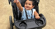 Osvaldo is registered to the contest to win money with this photo: baby, child, stroller, pointing, smiling, outdoor, denim_overall, white_shirt, blue_socks, black_stroller, babytrend, happy, infant, person, cute, seat, portrait, toddler, playful, daylight