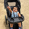 baby, child, stroller, pointing, smiling, outdoor, denim_overall, white_shirt, blue_socks, black_stroller, babytrend, happy, infant, person, cute, seat, portrait, toddler, playful, daylight