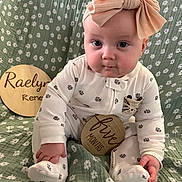 Raelyn is registered to the contest to win money with this photo: baby, infant, bow, headband, onesie, paw_prints, wooden_sign, five_months, green_blanket, floral_pattern, sitting, child, cute, portrait, milestone, indoor, person, soft_lighting, smiling, decor