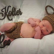 Kolter is registered to the contest to win money with this photo: newborn, baby, infant, knitted_clothing, bunny_ears, blanket, white_background, wooden_sign, name_sign, lying_down, cute, soft_texture, sleepy, hand, foot, hospital_bracelet, portrait, cozy, child, resting
