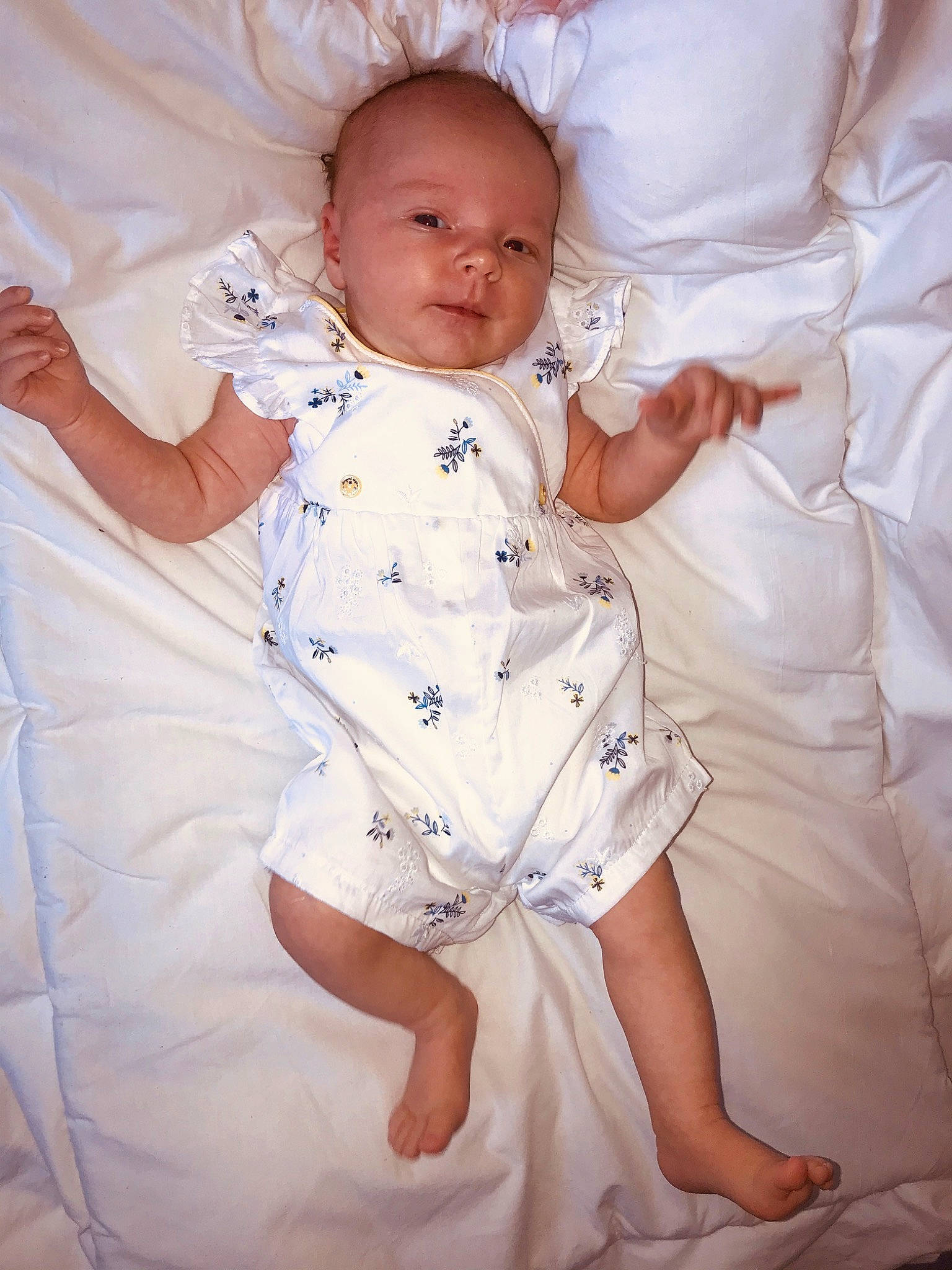 Jeanne participe au concours pour gagner de l'argent avec cette photo : arm, baby, baby_products, baby_toddler_clothing, bedding, child, dress, gesture, leg, linens, person, product, sitting, skin, smile, textile, toddler, white