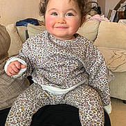 Aïcha participe au concours pour gagner de l'argent avec cette photo : baby, child, couch, cozy, curly_hair, cushion, eyes, fabric, feet, floral_pajamas, hands, indoor, lap, living_room, person, portrait, rosy_cheeks, sitting, smile, toddler