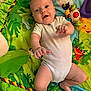 baby, infant, onesie, play_mat, toy, colorful, jungle_theme, green, smiling, cute, child, lying_down, indoors, happy, young, skin, face, hand, foot, play