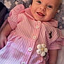 baby, infant, smiling, pink_dress, striped_clothing, buttoned_dress, toy, flower_toy, blanket, stars_pattern, cloud_pattern, lying_down, happy, cute, child, portrait, soft_texture, indoor, closeup, face