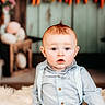 baby, child, boy, blue_clothing, bow_tie, suspenders, fluffy_rug, indoor, portrait, curious_expression, decorations, carrot_decor, rustic_background, soft_lighting, seated, cute, young_child, face, head, photography