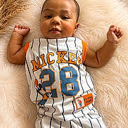Lamir is registered to the contest to win money with this photo: baby, infant, child, mickey_mouse, clothing, sportswear, jersey, shorts, smiling, lying_down, fluffy_rug, soft_texture, cute, portrait, indoor, comfortable, casual, person, baby_garment, relaxed