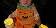 Roman is registered to the contest to win money with this photo: baby, pumpkin_costume, orange, green, striped_clothing, hat, candles, glowing, dark_background, cute, holiday, halloween, infant, sitting, face, eyes, hands, feet, plush, costume
