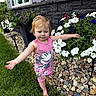 barefoot, child, cute, flower_bed, flowers, garden, grass, greenery, minnie_mouse, nature, outdoor, person, pink_dress, plants, rocks, smiling, stone_wall, summer, toddler, window
