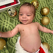 Giovanni is registered to the contest to win money with this photo: baby, infant, smiling, christmas, ornaments, green_blanket, holiday, festive, decorations, face, skin, cute, happy, lying_down, red_and_white_clothing, toddler, christmas_decor, celebration, joy, portrait