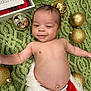 baby, infant, smiling, christmas, ornaments, green_blanket, holiday, festive, decorations, face, skin, cute, happy, lying_down, red_and_white_clothing, toddler, christmas_decor, celebration, joy, portrait