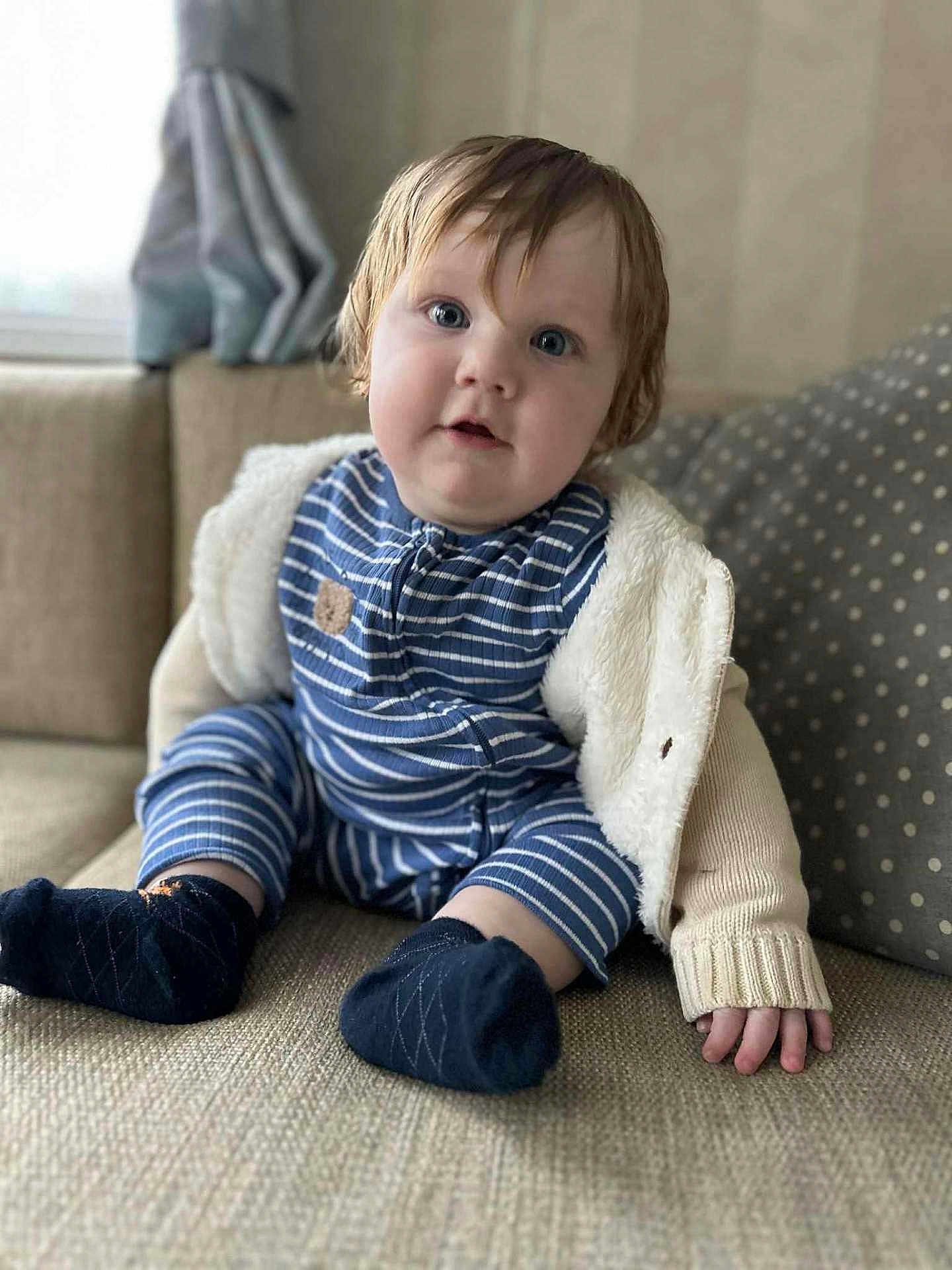 Freddie joined the competition — help win amazing prizes! baby, child, infant, blue_eyes, striped_pajamas, socks, couch, indoor, curly_hair, cozy_clothing, cute, seated, portrait, soft_texture, home, furniture, curious_expression, warm_light, casual, smiling