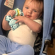 Raylin is registered to the contest to win money with this photo: baby, child, car_seat, toy, giraffe_toy, blue, white_shirt, light_blue_pants, infant, cute, smiling, indoor, seat_belt, person, holding, face, head, hands, clothing, floor