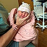 Olivia is registered to the contest to win money with this photo: newborn, baby, infant, hospital, blanket, hat, person, hand, skin, clothing, seated, furniture, medical_equipment, indoors, cute, portrait, holding, pink, teddy_bear, care