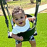 baby, child, swing, playground, outdoor, grass, smiling, happy, curly_hair, white_shirt, shorts, sunny, park, seat, metal_chains, cute, infant, person, summer, fun