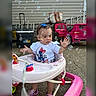 toddler, baby, walker, bubbles, outdoor, toy_car, purple_shoes, white_shirt, blue_bow, playtime, child, curious, concrete_ground, plastic_toy, open_car_door, red_bracelet, summer, daylight, background, fun
