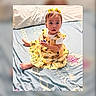 Sahara joined the competition — help win amazing prizes! baby, child, yellow_dress, bow, bed, pillow, patterned_bedspread, sitting, curious, indoors, cute, holding_object, short_hair, barefoot, portrait, infant, clothing, soft_lighting, person, young_child