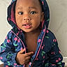 Ariyah joined the competition — help win amazing prizes! toddler, child, portrait, smiling, hood, jacket, raincoat, cherry_pattern, floral_pattern, sitting, indoors, face, eyes, hair, hands, clothing, wood_floor, wall, photography, cute
