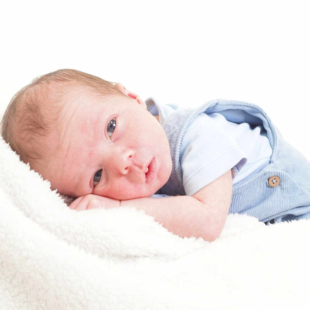 Euan is registered to the contest to win money with this photo: baby, blanket, blue_clothing, child, cozy, cute, face, head, indoors, infant, lying_down, newborn, peaceful, person, portrait, resting, skin, sleepy, small, soft