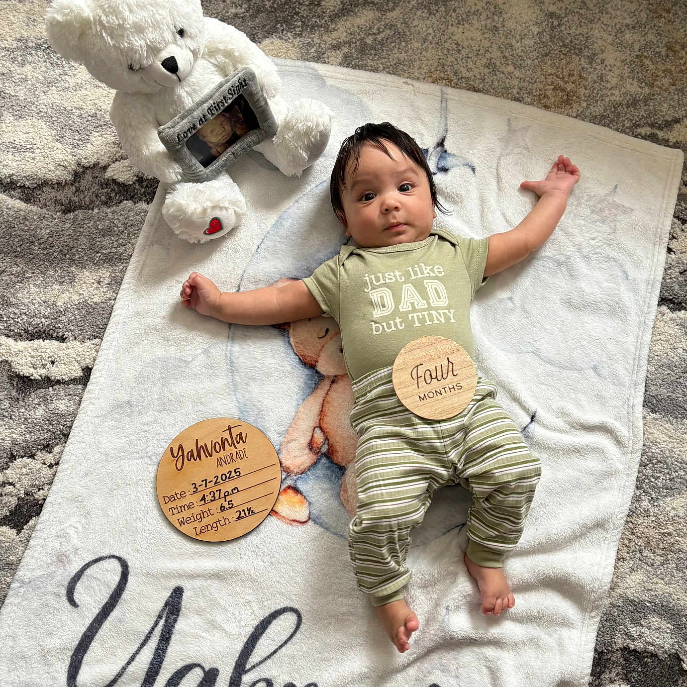 Yahvonta is registered to the contest to win money with this photo: baby, baby_boy, baby_milestone, blanket, child, clothing, cute, face, floor_rug, home_interior, infant, lying_down, newborn, person, portrait, script_text, soft_toy, striped_pants, teddy_bear, wooden_plaques