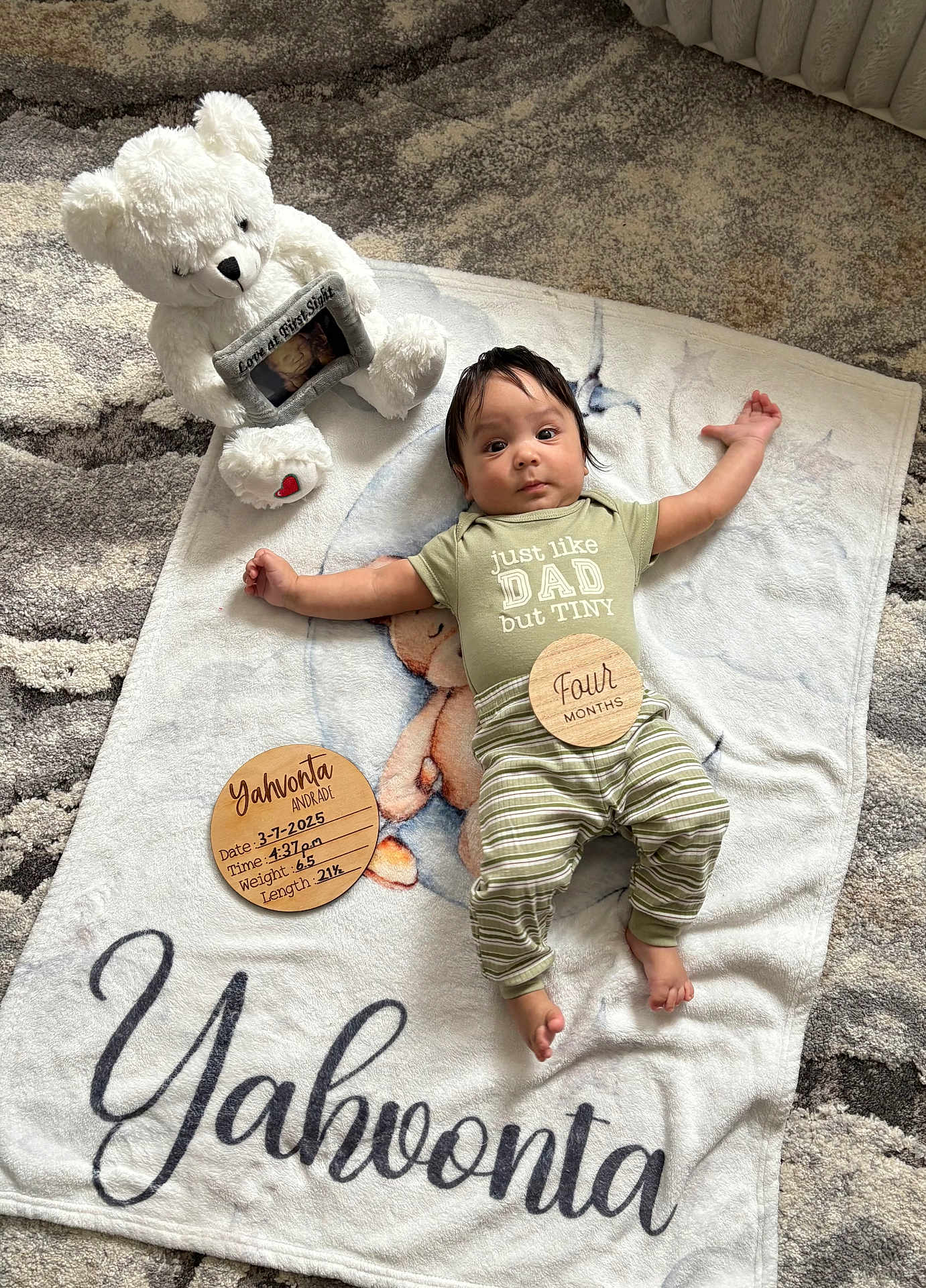 Yahvonta is registered to the contest to win money with this photo: baby, blanket, teddy_bear, wooden_plaques, infant, person, clothing, striped_pants, floor_rug, cute, portrait, baby_milestone, lying_down, home_interior, soft_toy, baby_boy, script_text, face, newborn, child