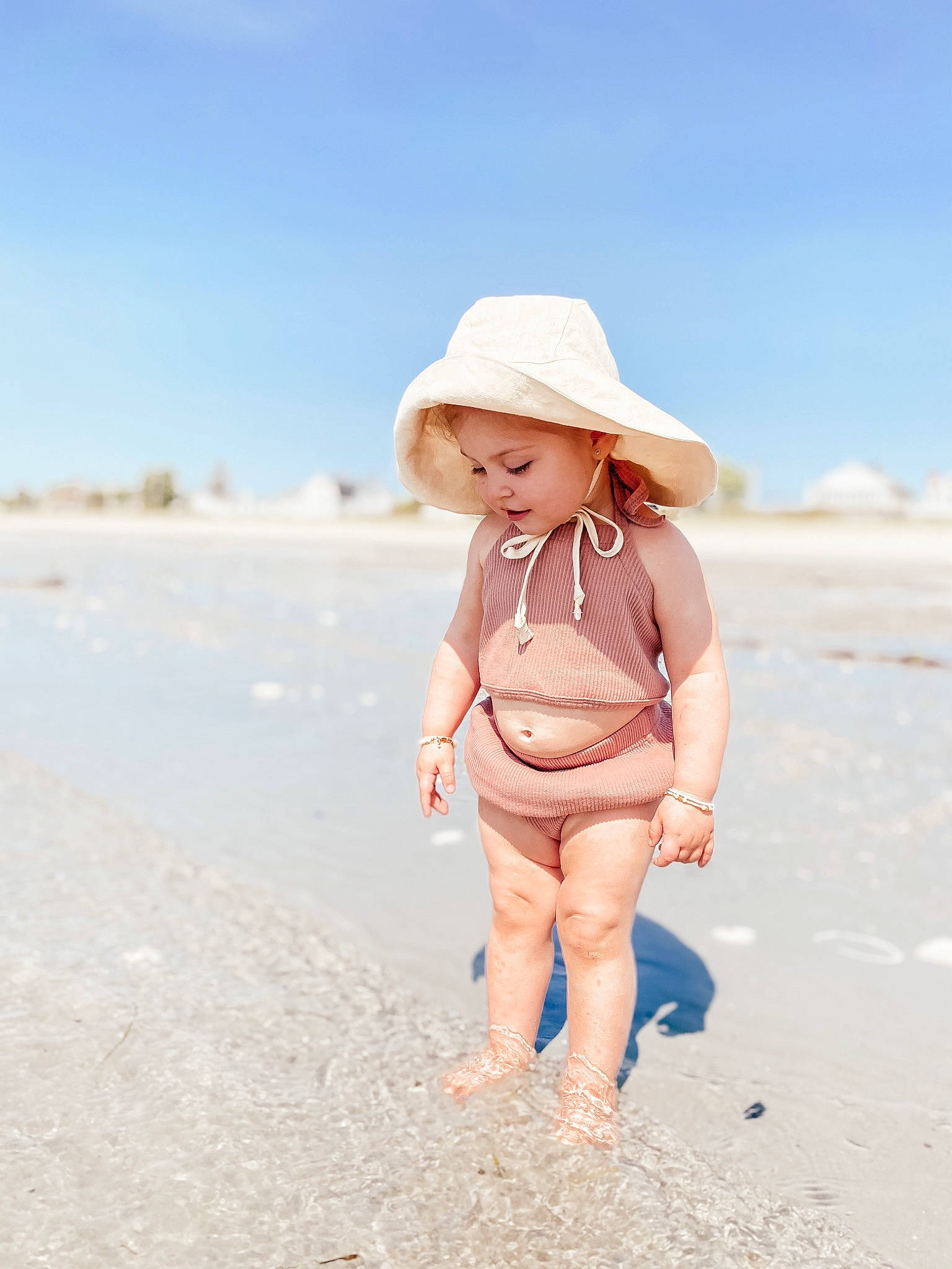 Thea is registered to the contest to win money with this photo: baby, beach, blond, coastal_and_oceanic_landforms, fedora, happy, hat, headgear, headwear, human_body, human_leg, landscape, people_in_nature, people_on_beach, person, sand, shore, sky, sun_hat, swimwear