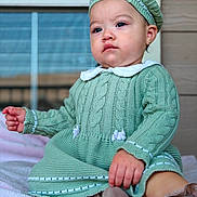 Megan Garcia is registered to the contest to win money with this photo: baby, child, knitted_clothing, beret, green_outfit, sitting, blanket, window, indoor, portrait, cute, face, earring, soft_toys, expression, person, footwear, hand, furniture, cozy