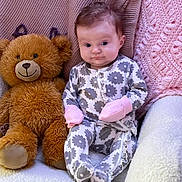Amelia joined the competition — help win amazing prizes! baby, teddy_bear, blanket, onesie, mittens, soft_texture, cute, infant, seated, plush_toy, patterned_clothing, indoor, cozy, child, portrait, smile, face, furniture, comfort, pink