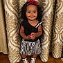Julia is registered to the contest to win money with this photo: toddler, child, smile, black_top, striped_shorts, heart_pattern, headband, red_flower, curtain, patterned_curtain, white_sandals, wooden_floor, standing, indoors, happy, cute, person, portrait, fashion, toy