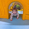 toddler, child, playground, yellow_tunnel, crawling, blue_floor, indoor_play_area, happy, smiling, playtime, fun, colorful, plastic, floor_texture, young_child, casual_clothing, curly_hair, active, exploring, daylight