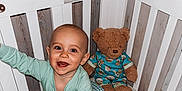 John joined the competition — help win amazing prizes! baby, crib, teddy_bear, pajamas, smile, happy, child, indoor, furniture, toy, cushion, person, wood, playful, infant, cute, sleepwear, childrens_room, reaching, portrait