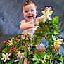 baby, child, smiling, flowers, greenery, playful, happy, portrait, indoor, cute, infant, white_clothing, decorative_plants, sitting, bright_eyes, cheerful, soft_background, colorful, nature_theme, young_child