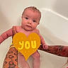 Lilly is registered to the contest to win money with this photo: baby, bathtub, tattooed_arms, water, child, infant, person, skin, holding, cute, naked, bath_time, love, heart_shape, text_overlay, red_shirt, human, portrait, indoors, parent