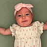 Evie is registered to the contest to win money with this photo: baby, infant, headband, pink, dress, floral, arms, lying_down, green_background, cute, smiling, child, portrait, soft_texture, happy, face, skin, person, toddler, clothing