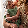 baby, infant, smile, headband, bow, green_outfit, arms, holding, adult, person, happy, portrait, closeup, clothing, skin, indoor, curtain, light, tattoo, flower_pattern