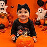baby, child, halloween, pumpkin, jack_o_lantern, costume, bow_headband, smiling, portrait, indoor, orange_background, ghost_decorations, bat_decorations, balloons, autumn_leaves, black_clothing, festive, seasonal, candle, studio_photography