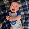 baby, smiling, infant, blanket, plaid, blue, gray, onesie, clothing, happy, cute, lying_down, portrait, child, skin, hand, face, head, indoor, playful