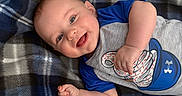 Jaxson is registered to the contest to win money with this photo: baby, smiling, infant, plaid_blanket, blue, gray, shirt, baseball_glove, baseball, happy, lying_down, cute, child, portrait, indoors, soft_texture, clothing, person, closeup, skin