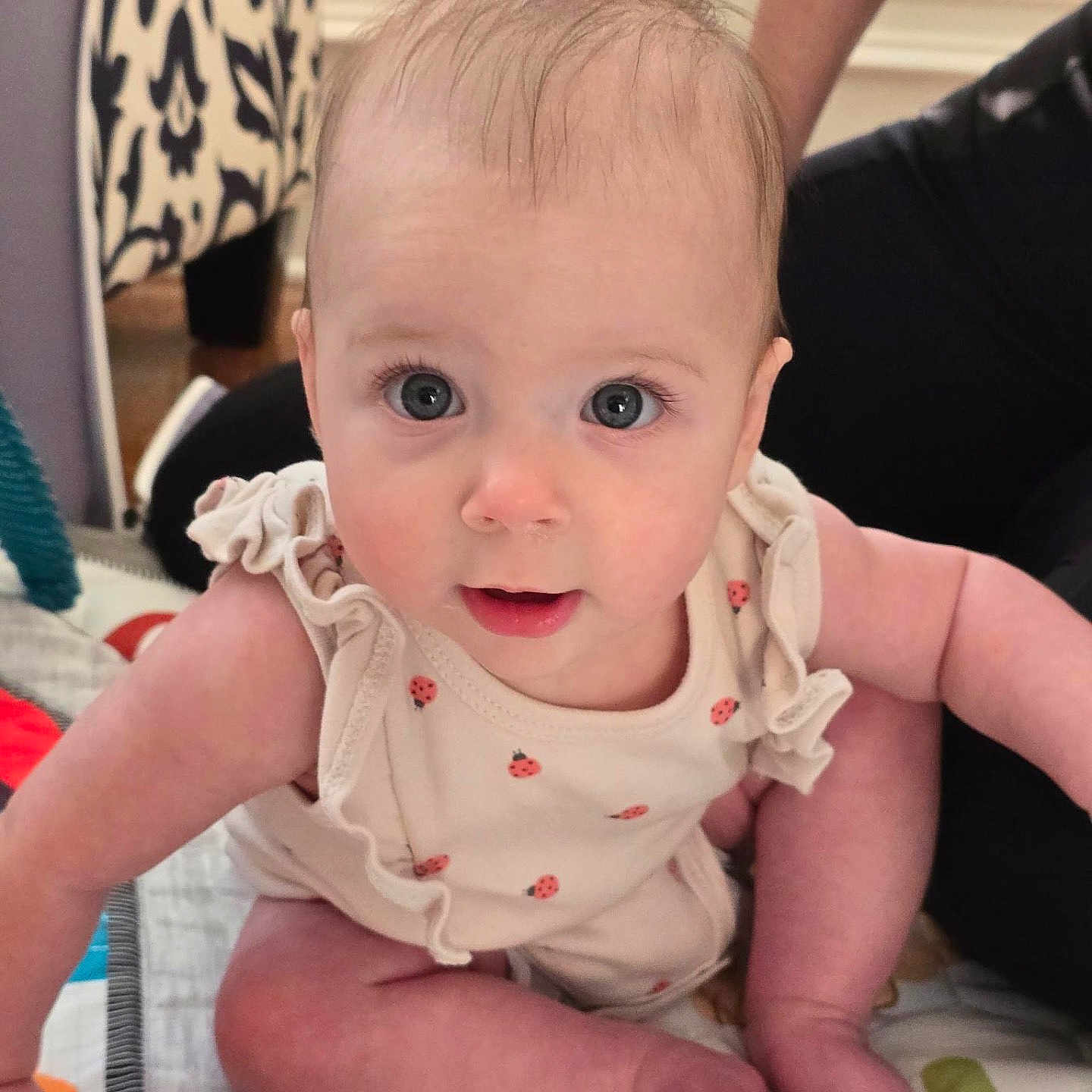Eden joined the competition — help win amazing prizes! baby, infant, child, cute, blue_eyes, sitting, clothing, ladybug_pattern, quilt, furniture, person, indoor, curious, face, skin, hair, foot, hand, expression, home
