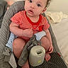 Moses is registered to the contest to win money with this photo: baby, baby_seat, barefoot, child, closeup, comfortable, curly_hair, cute, gray_fabric, home, indoor, infant, person, portrait, puzzled_expression, red_onesie, sitting, soft_toy, striped_clothing, young_child