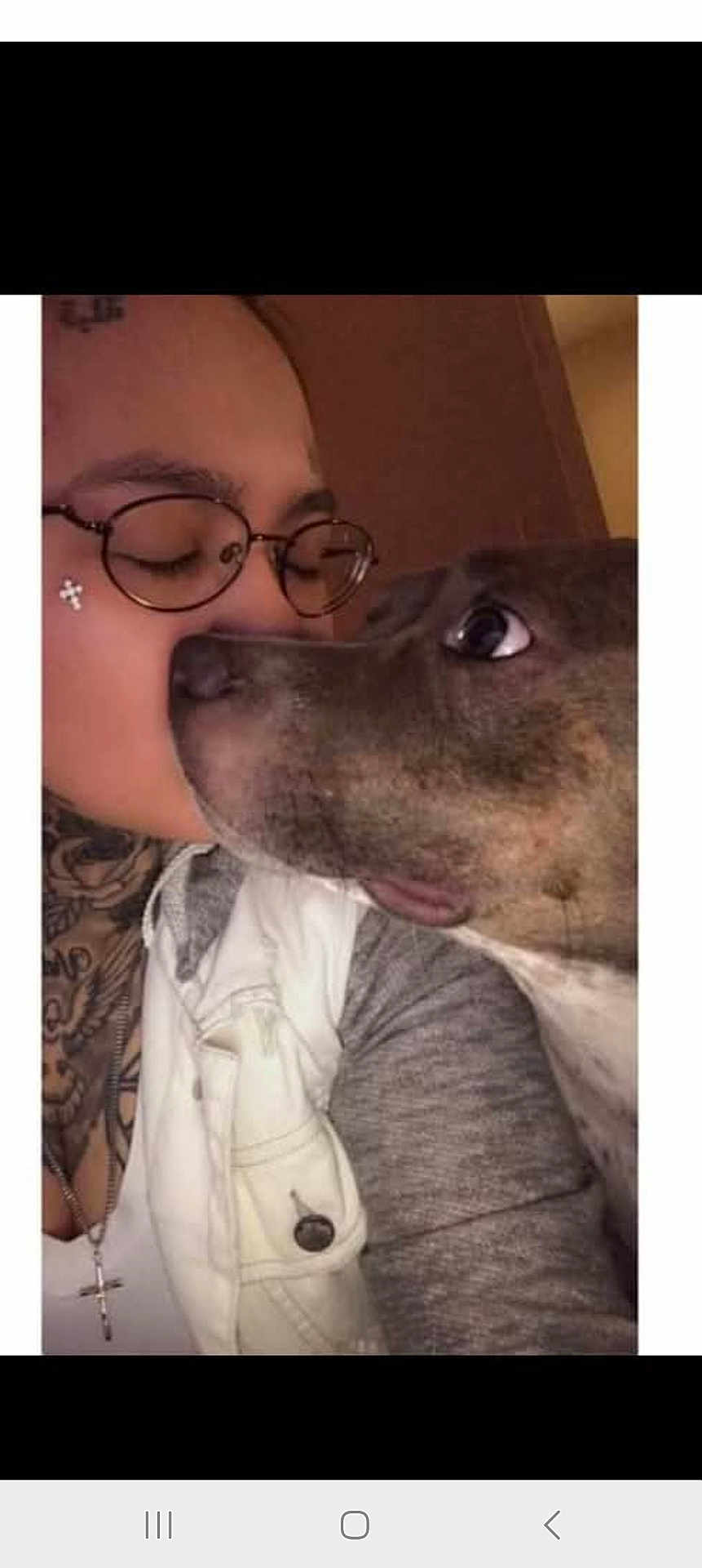 Gia joined the competition — help win amazing prizes! person, dog, glasses, tattoo, close_up, indoor, affection, nose_to_nose, curious, warm_lighting, casual_clothing, gray_sweater, white_jacket, cross_necklace, pet, bond, face, animal, human, intimate