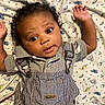baby, infant, curly_hair, overalls, gray_shirt, blanket, pattern, smiling, face, eyes, arms_up, cute, child, portrait, lying_down, fabric, clothing, happy, indoor, person