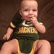 Lainee is registered to the contest to win money with this photo: baby, infant, child, smiling, sitting, green_bay_packers, onesie, clothing, couch, furniture, hand, face, eyes, skin, person, indoors, cute, happy, portrait, baby_fashion