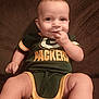 baby, infant, child, smiling, sitting, green_bay_packers, onesie, clothing, couch, furniture, hand, face, eyes, skin, person, indoors, cute, happy, portrait, baby_fashion