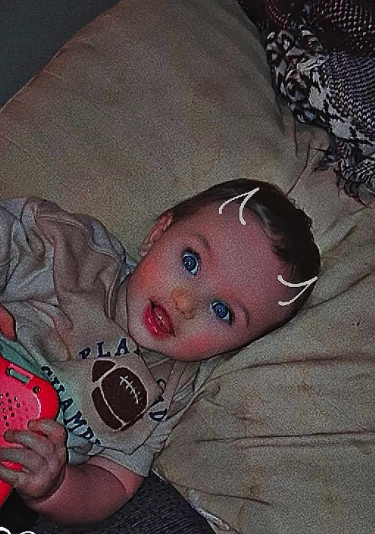 Jerry is registered to the contest to win money with this photo: baby, infant, child, blue_eyes, pillow, blanket, toy, hand, tshirt, football_graphic, lying_down, portrait, smile, cheeks, doodle_marks, fabric, sofa, ear, hair, indoor