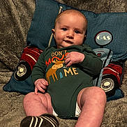 Wyatt is registered to the contest to win money with this photo: baby, infant, onesie, green_clothing, pillow, couch, fabric, socks, smile, face, hand, legs, footwear, indoor, child, cute, plush, comfort, relaxing, portrait