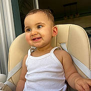 Mélia participe au concours pour gagner de l'argent avec cette photo : toddler, child, high_chair, white_tank_top, smiling, face, skin, arm, indoor, window, straps, curly_hair, seat, baby, happy, closeup, person, cute, expression, looking_away