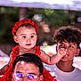 baby, child, man, teenager, red_dress, flower_headband, glasses, curly_hair, outdoor, portrait, people, smiling, shoulders, reaching_hand, background_blur, daylight, family, happy, casual_clothing, nature